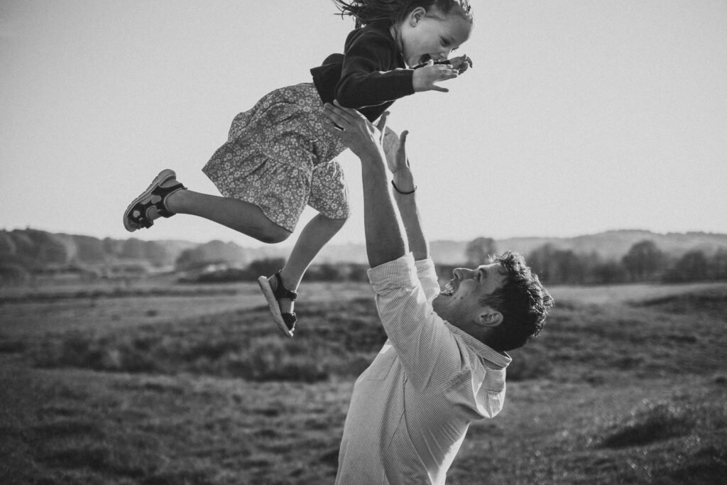 Vater hebt Tochter hoch über seinen Kopf, beide lachen bei einem Familienfotoshooting in Flensburg