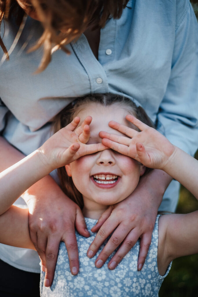 Mädchen hält sich lachend die Hände vor die Augen, Muter steht hinter ihr - Outdoor Fotoshooting aus Flensburg