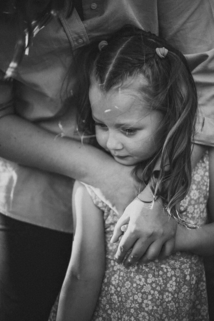 Portrait eines Mädchens in den Armen seiner Mutter in schwarz weiß - Natürliches Familienfoto aus Flensburg.