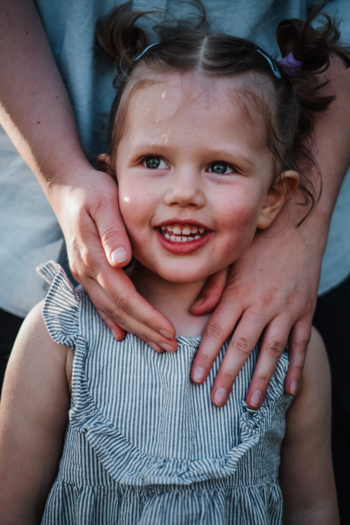 Portrait eines Mädchens mit Händen der Mutter am Gesicht, aufgenommen von einer Flensburger Fotografin.