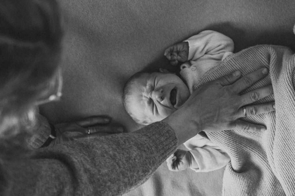 Mutter legt Hand auf die Brust des schreienden Säuglings - Neugeborenen Homestory Flensburg.