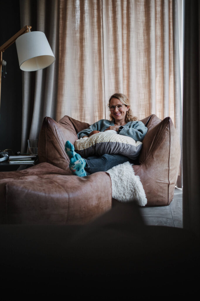 Mutter stillt ihr Baby auf einem Sessel zu Hause _ Fotografin für Neugeborene Flensburg