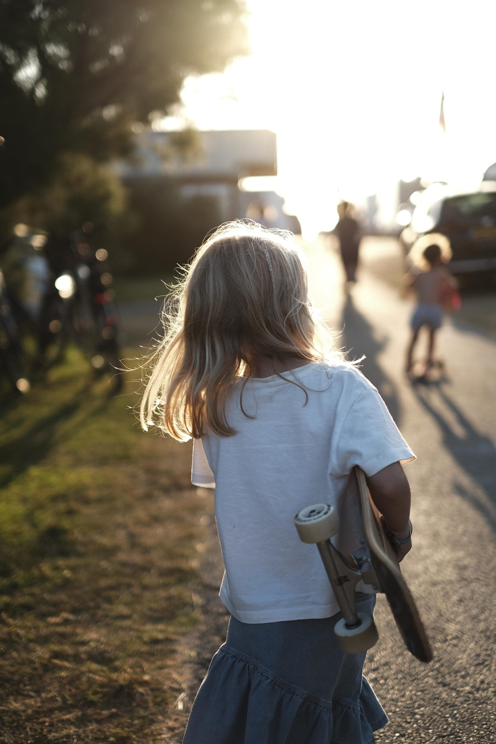 Mädchen mit Skateboard unter dem Arm, steht vor dem Sonnenuntergang