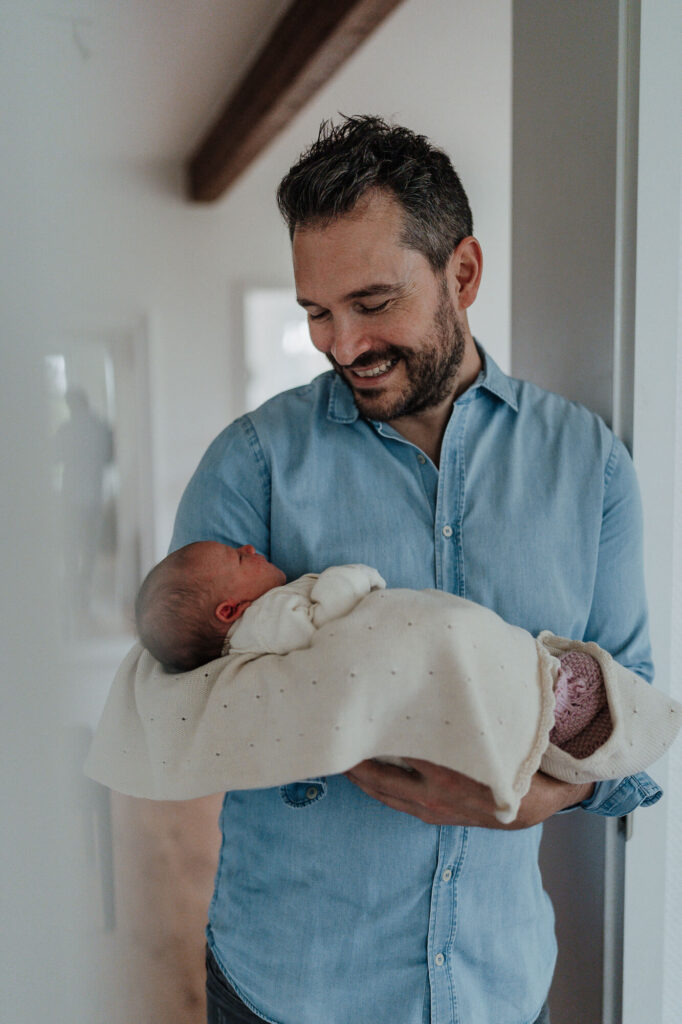 Vater hält sein Neugeborenes im Türrahmen zu Hause – Neugeborenen Homestory aus Flensburg.