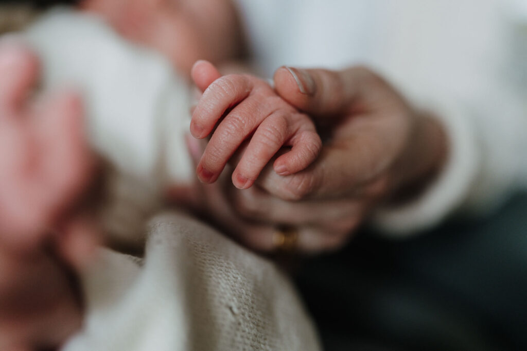 Die zarten Hände des Neugeborenen in der Hand der Mutter, aufgenommen von einer Neugeborenen Fotografin in Flensburg.