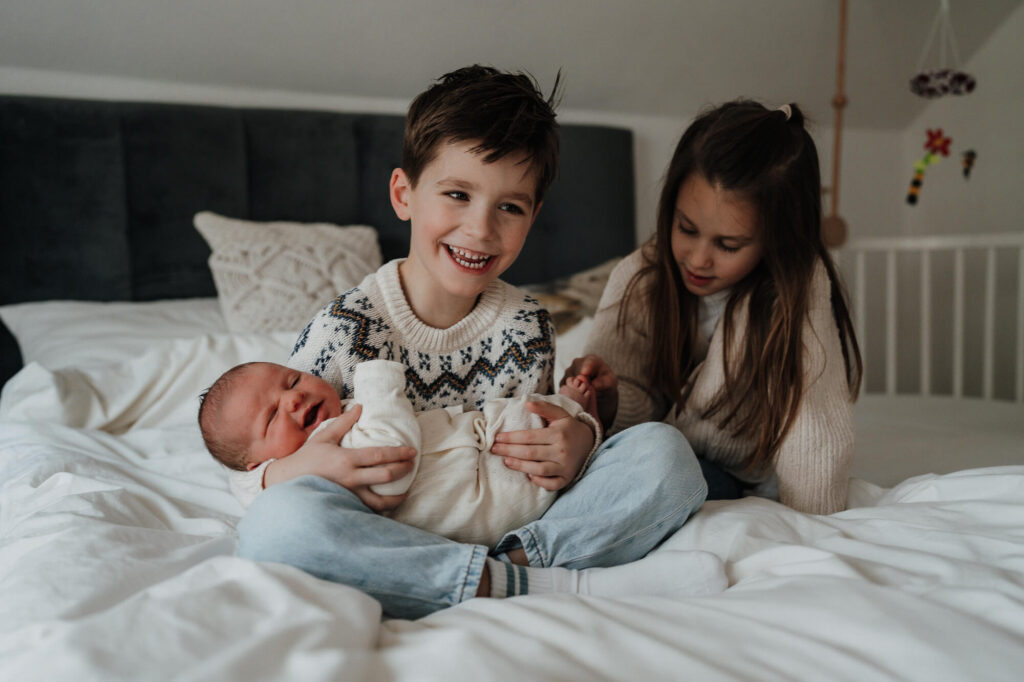 Geschwister halten ihr Neugeborenes im Schoß – Familienfotoshooting in Flensburg.