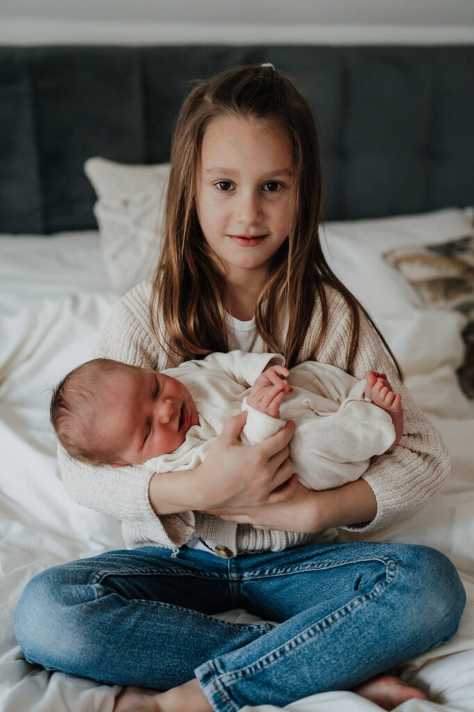 Älteres Geschwisterkind hält Neugeborenes im Schoß – Familienfotoshooting in Flensburg
