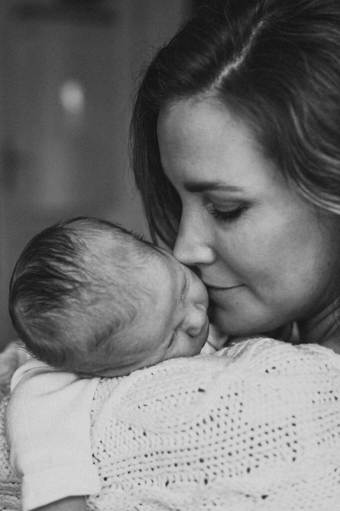 Portrait einer Mutter mit Neugeborenem auf der Schulter. Sie liebkost das Baby bei einem Shooting in Flensburg.