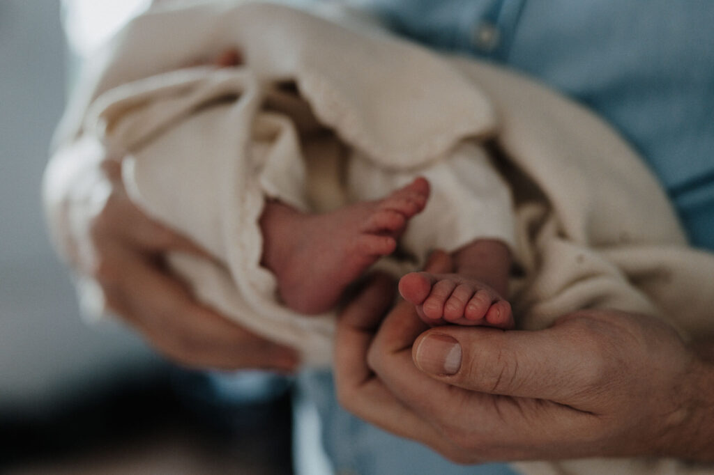 Babyfüße im Arm des Vaters, Nahaufnahme bei einem Neugeborenen Fotoshooting in Flensburg.