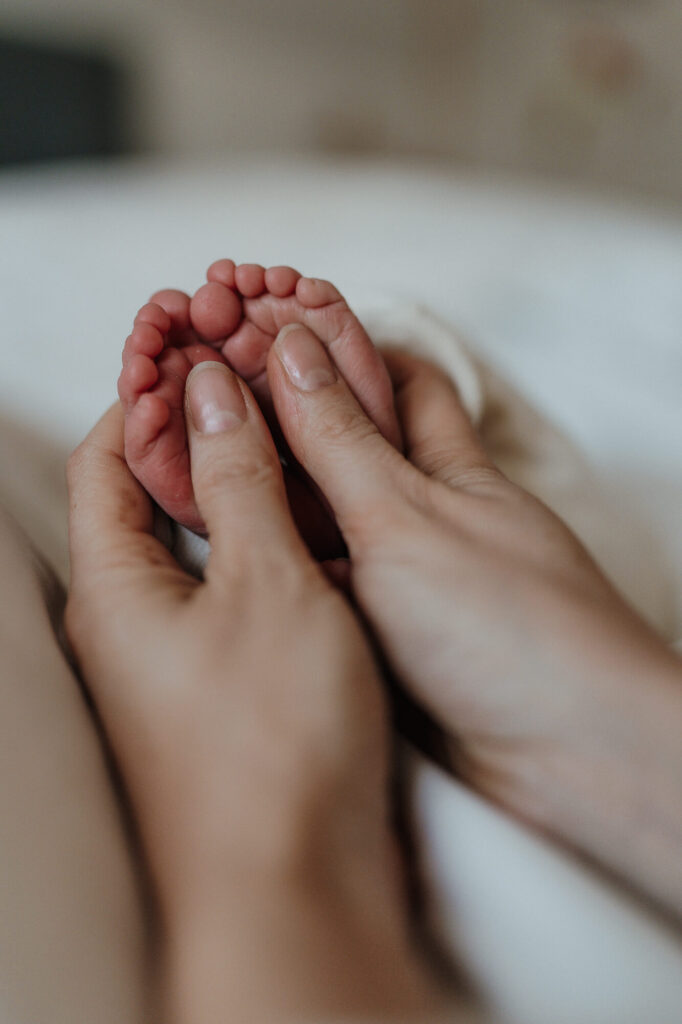 Nahhaufnahme von Babyfüßen in Händen der Mutter. Das Bild entstand bei einem Neugeborenen Shooting in Flensburg bei der Familie zu Hause.