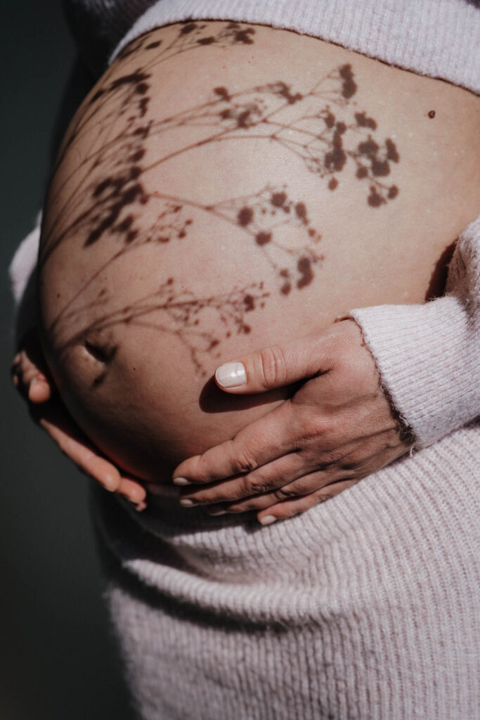 Nahhaufnahme eines Babybauchs mit dem Schatten einer Pflanze