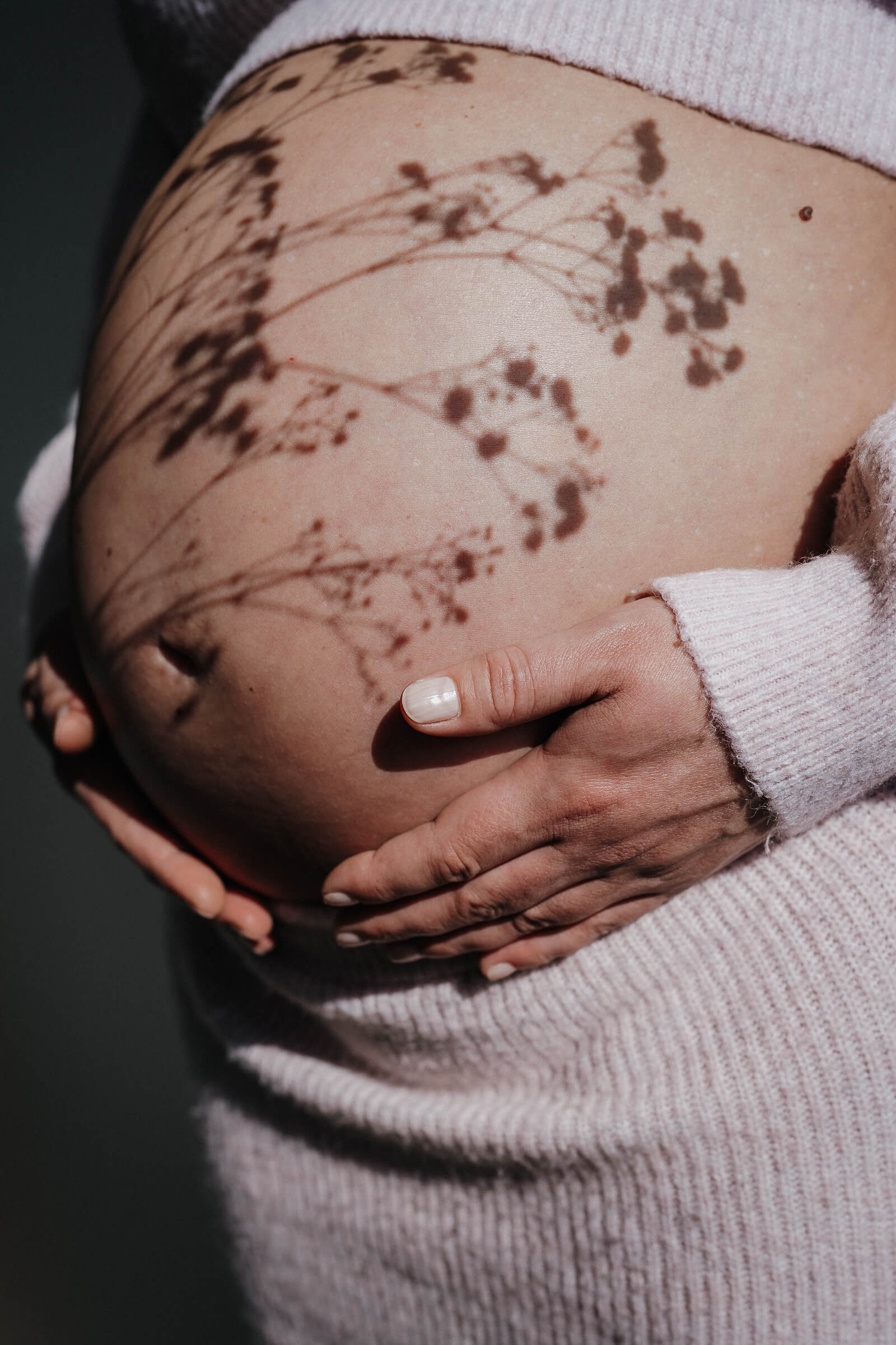 Nahhaufnahme eines Babybauchs mit dem Schatten einer Pflanze