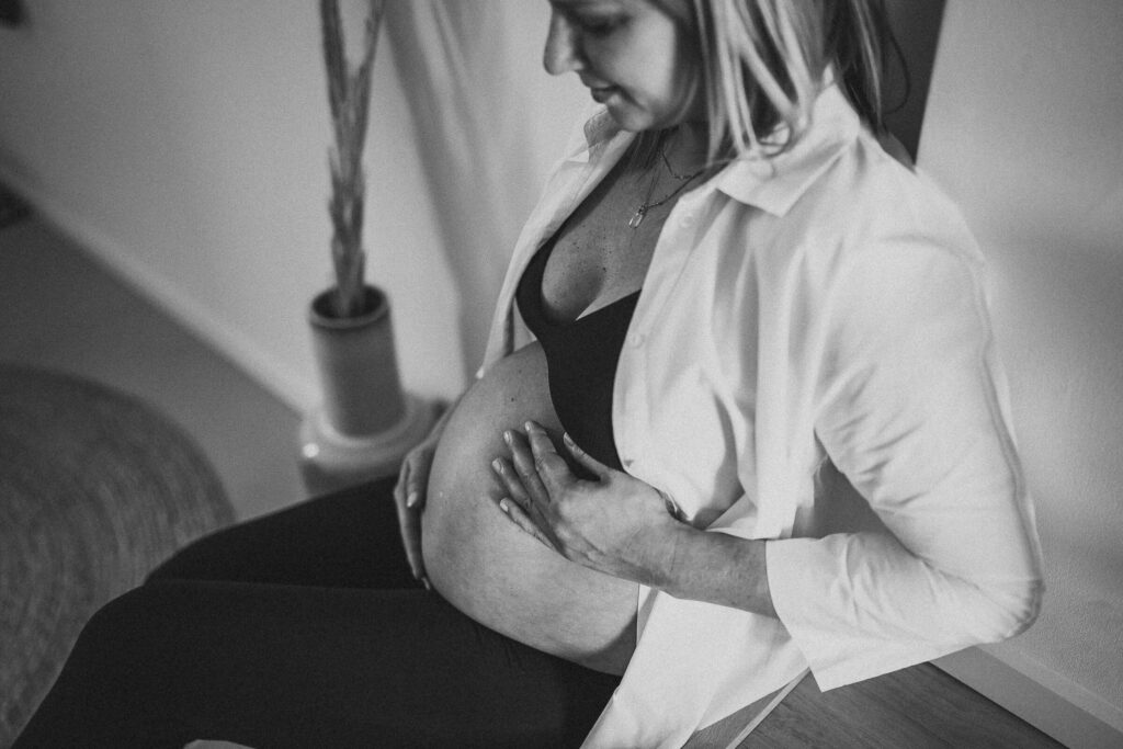 Werdende Mama hält ihren Babybauch und sitzt auf einer Treppe in ihrem zu Hause