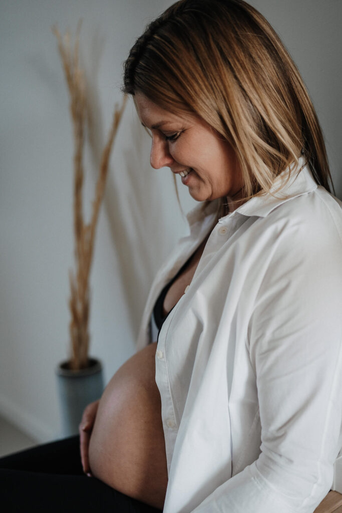 Schwangere Frau mit offener Bluse lacht herunter zu ihrem Babybauch