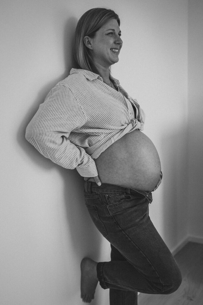 Schwarz weiß Foto von einer Frau mit Babybauch in Flensburg an eine Wand gelehnt
