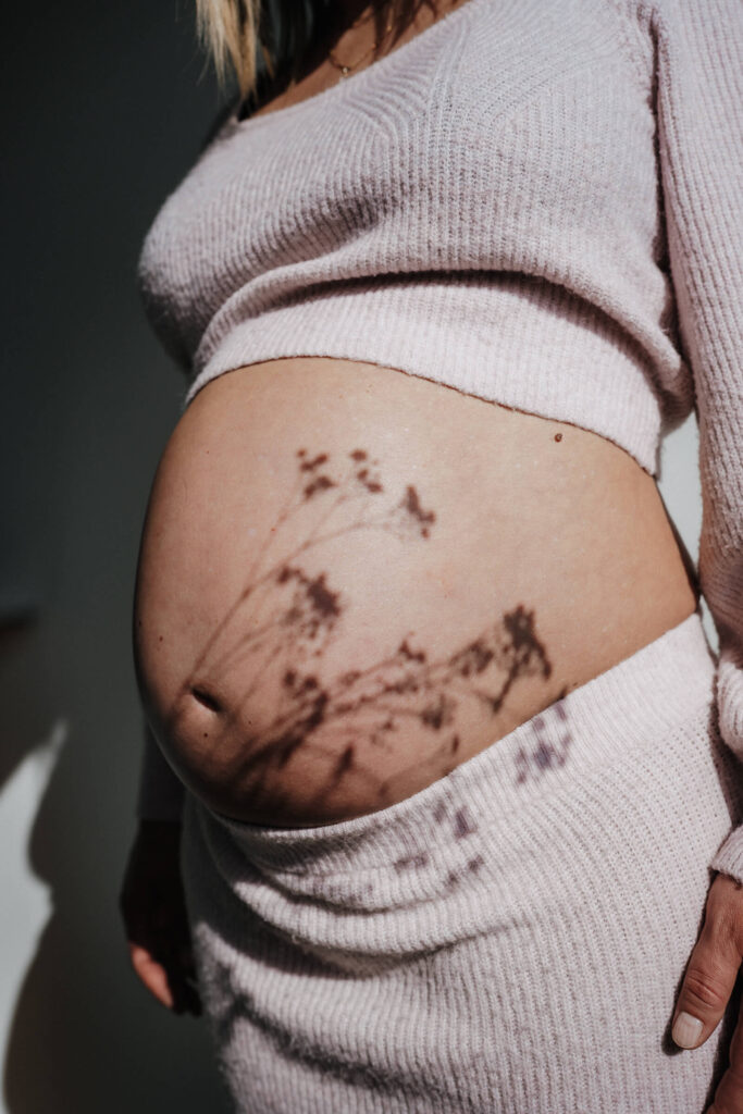 Nahaufnahme eines Babybauchs mit dem Schatten einer Blume darauf