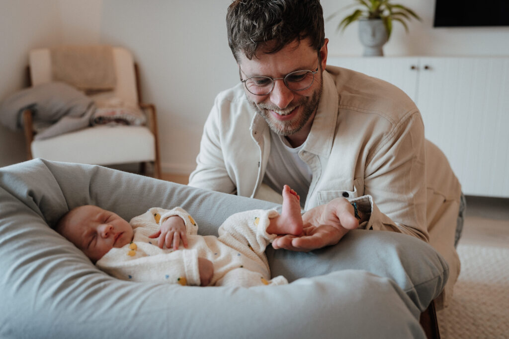 Vater betrachtet entzückt die winzigen Babyfüße bei einem Newborn Shooting