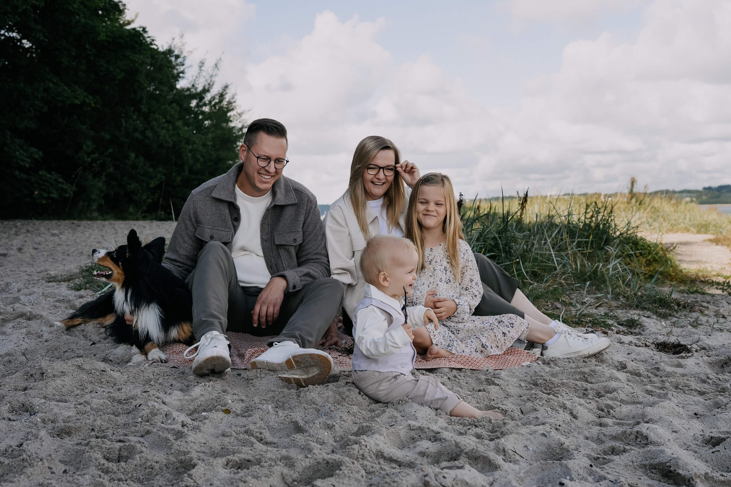 Familienfoto mit Hund auf einer Decke am Strand
